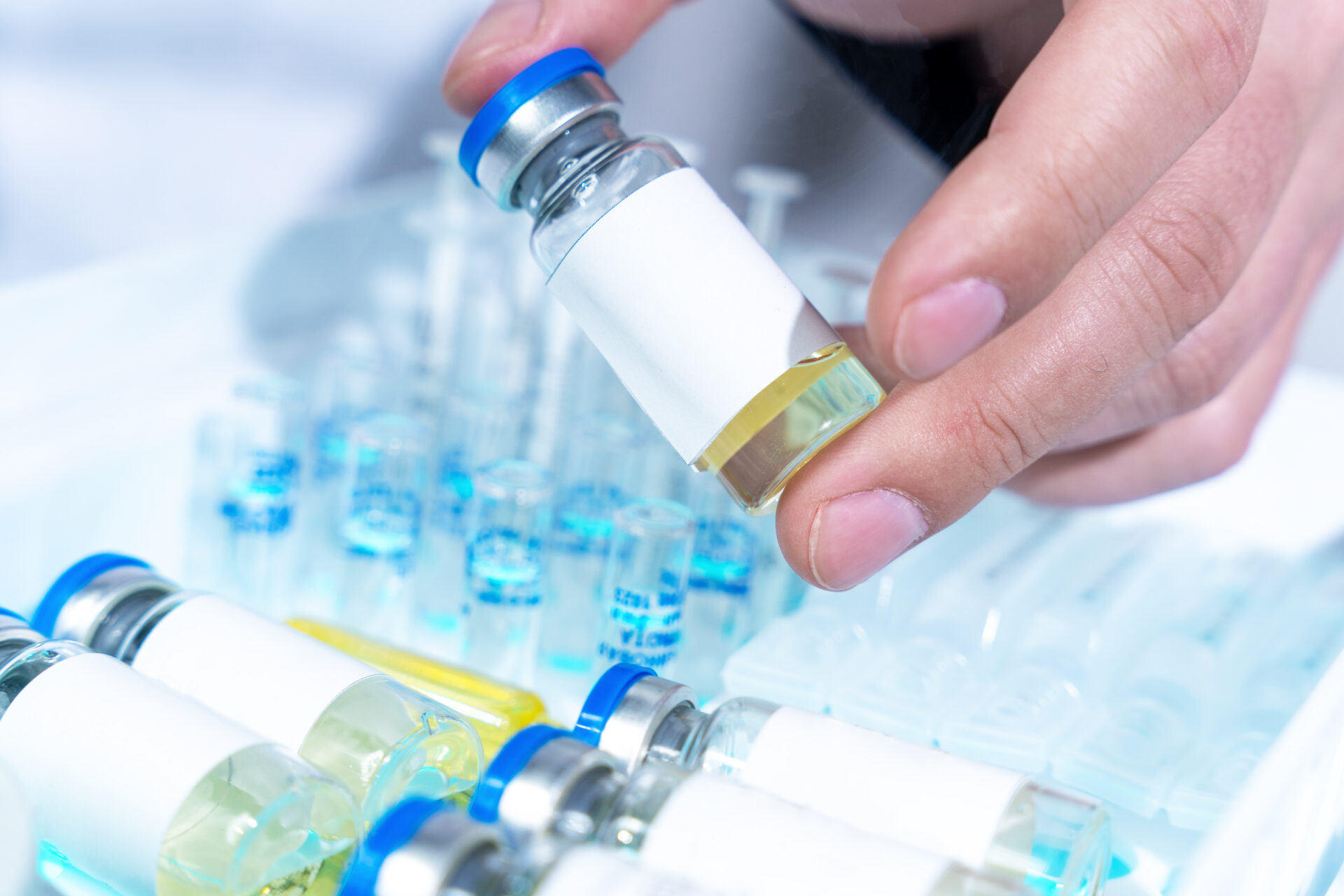 Hand holding vial with blue cap and liquid.