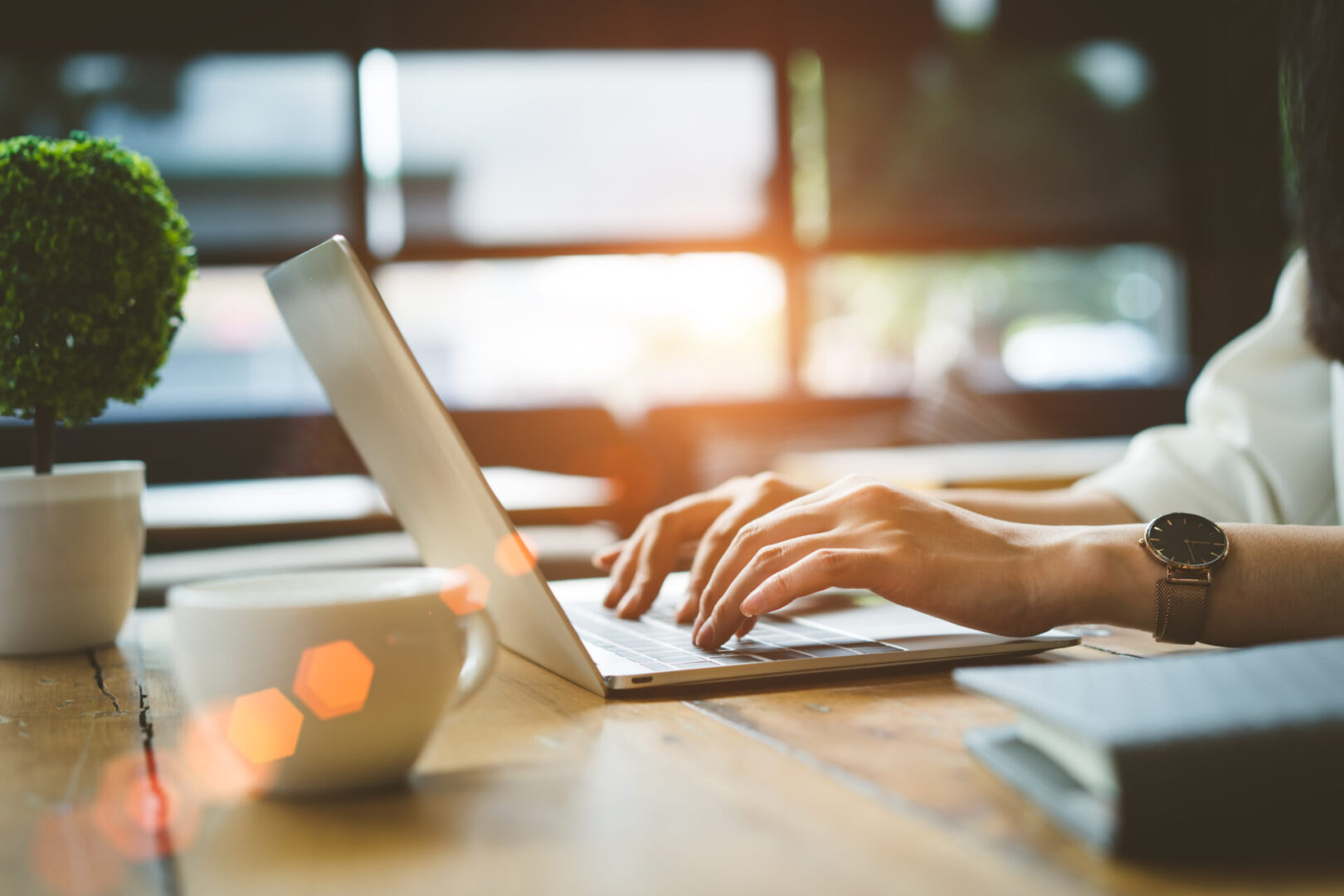 Woman typing on laptop with coffee cup.