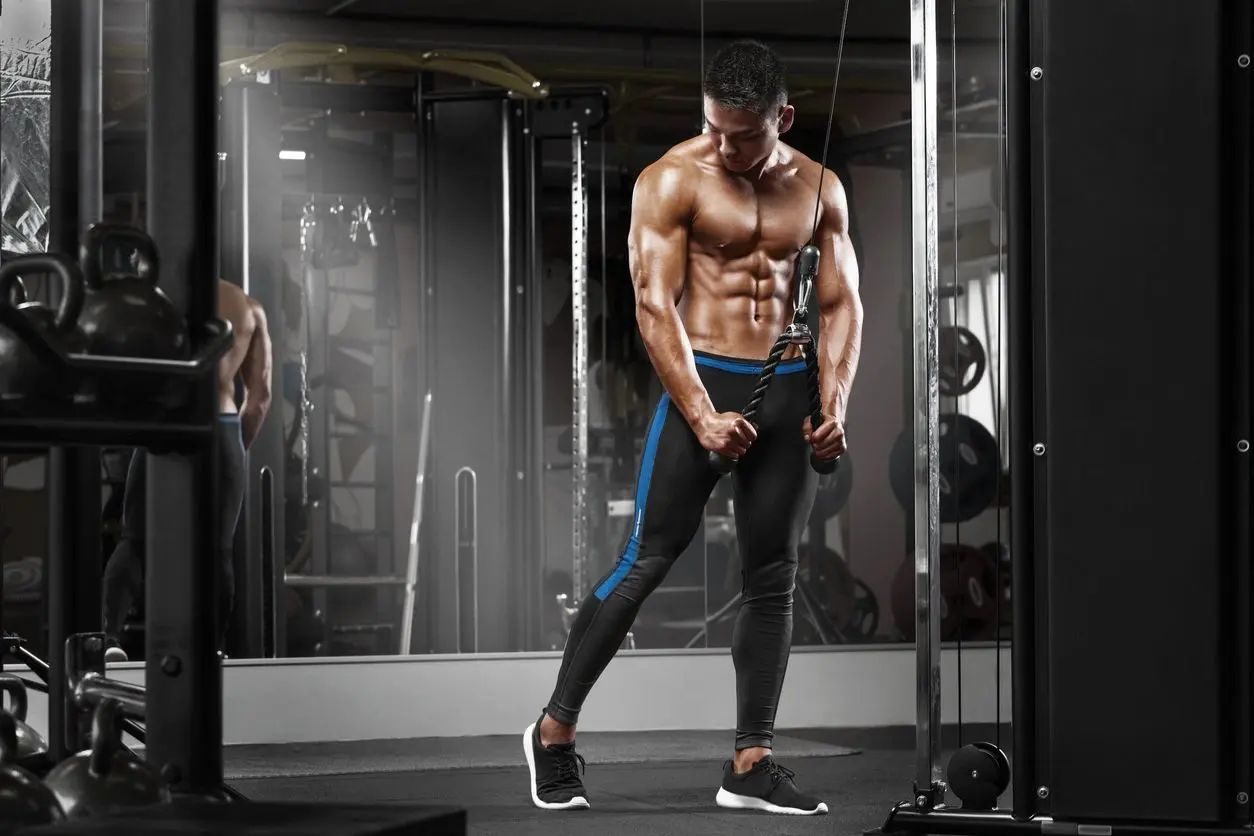 A man is standing in the gym with his hands on the handles.