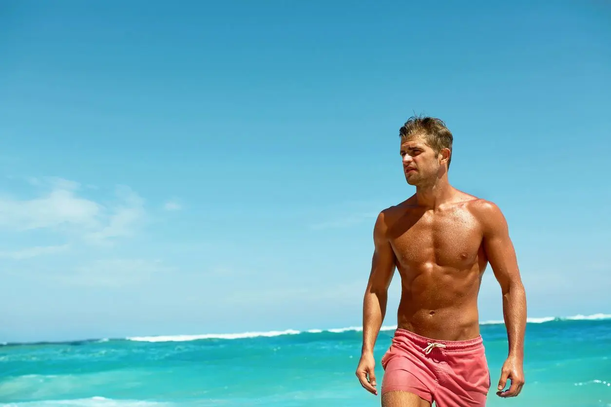 A man in swim trunks standing on the beach.