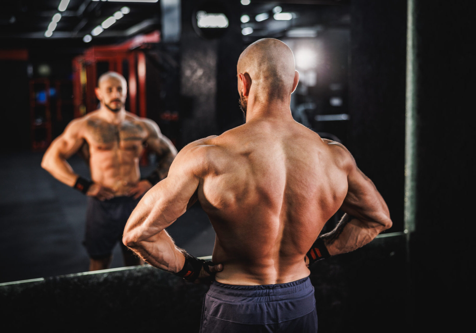 Muscular man looking at reflection in gym.